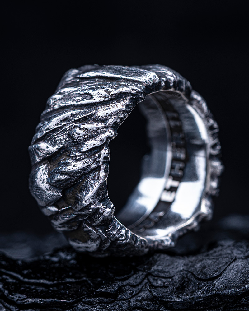 Stone Cliff Band photographed against a black background, its carved silver ridges lit in high contrast.