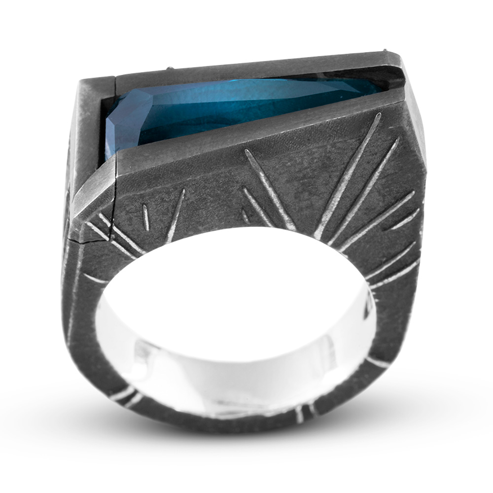 Side view of the Momentum Ring showing the sunburst engraving across the oxidized silver shoulder and the tapered blue stone above.